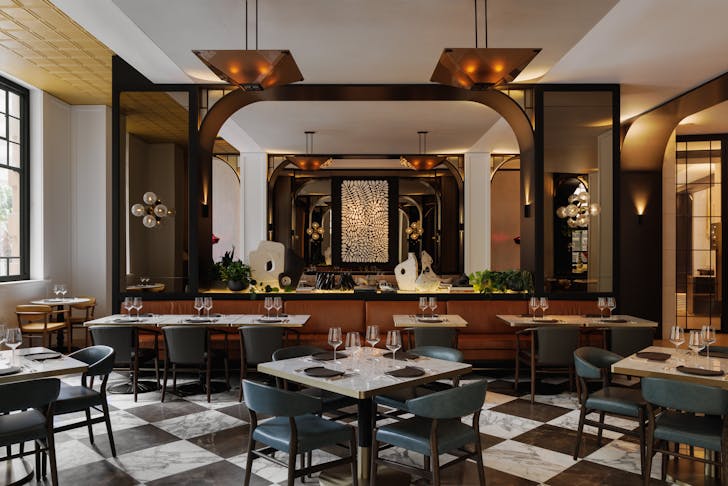 Interior of Brasserie 1930, black and white marble checkered floors, white square tables and at the back an orange booth with tables facing