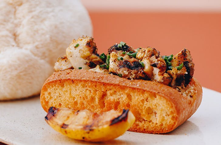 Grilled lion's mane mushrooms inside a crusty piece of bread with a grilled slice of lemon 