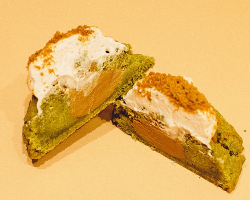 Two halves of a matcha cookie stuffed with biscoff and topped with strawberry cream. 