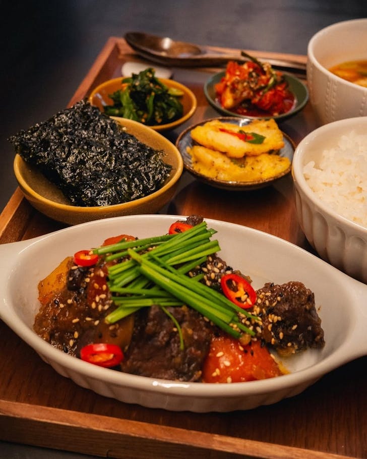A wooden tray artifully arranged with Korean short ribs, rice, kimchi and other side dishes.