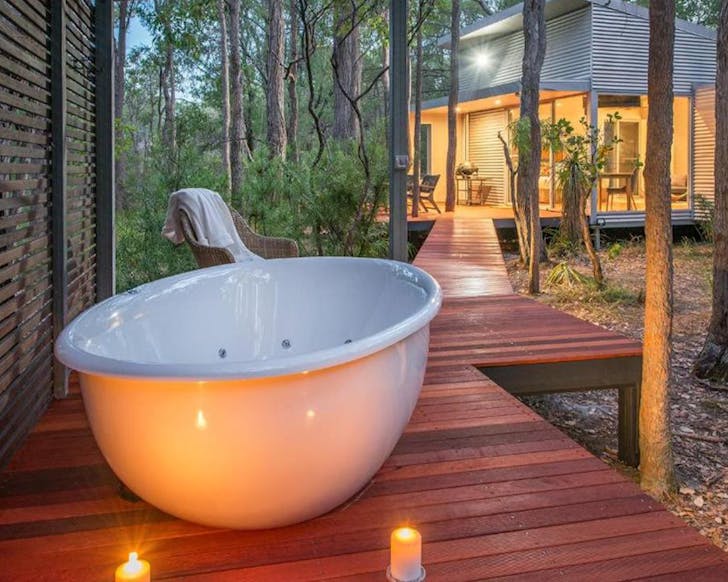 A tub on a private deck surrounded by bush
