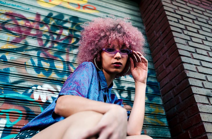 A girl poses outside a graffitied garage.