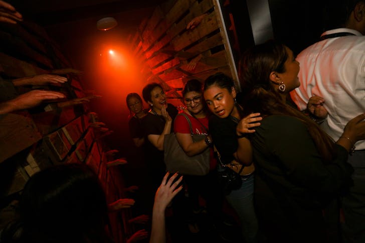 People in a spooky corridor washed in red lighting at Halloween Horror Nights 10 at Universal Studio Singapore. A person in costume scares them. 