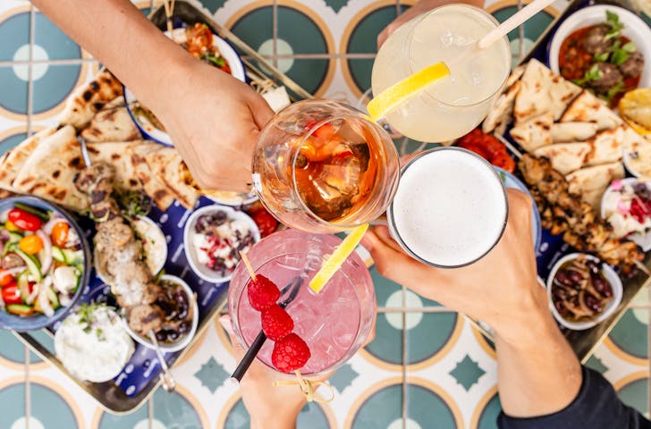 hands holding glasses over a food spread